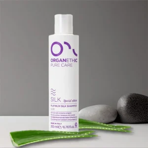 White bottle of shampoo- Platinum silk shampoo standing amongst aloe-vera leaves.