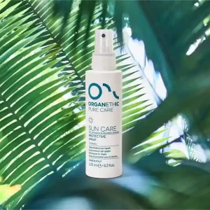 A bottle of sun care protective hair spray standing on a palm leaf.