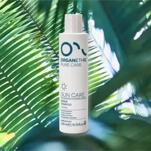 A bottle of sun care repair shampoo standing on a palm leaf